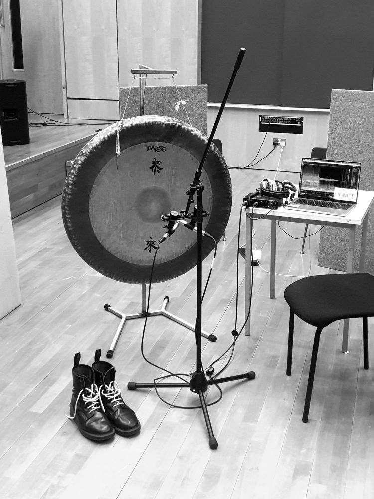 Tam tam on a stand in the studio, with XY microphones and boots abandoned in front of it.