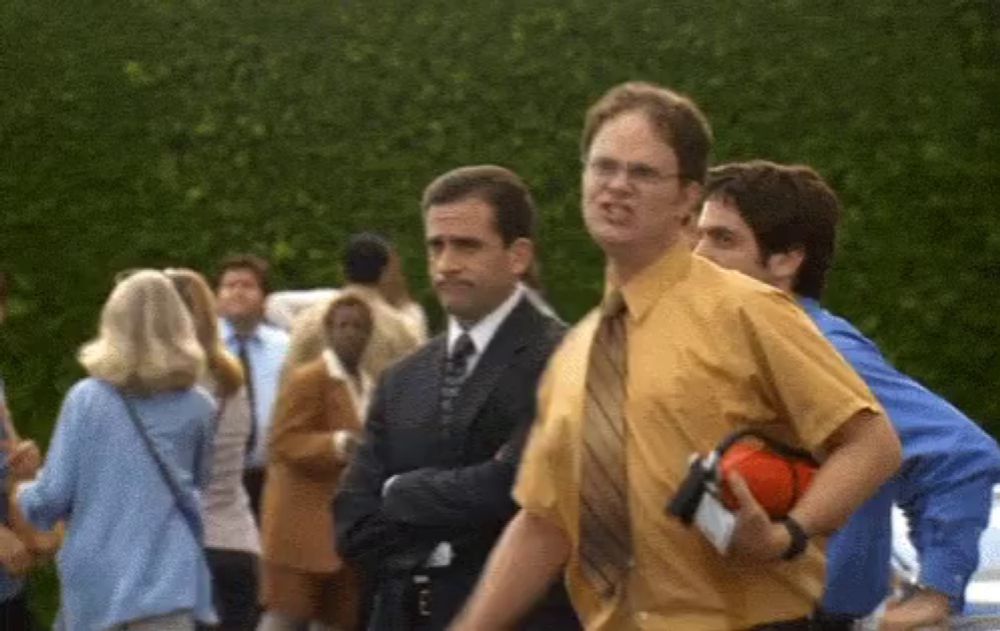 a man in a yellow shirt and tie stands in a crowd of people .