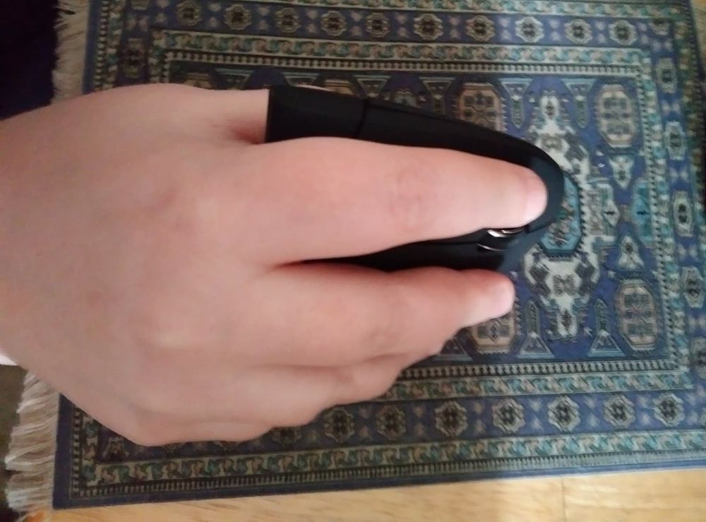 Photo of a hand holding a vertical mouse on a blue mousepad shaped like a rug.