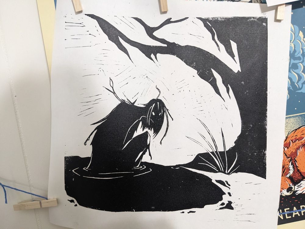 A print in black and white hanging on a wall via yarn and clothes pins, drying. The image is of a shadowed creature emerging from murky water beside a tree with Spanish moss on its branches.