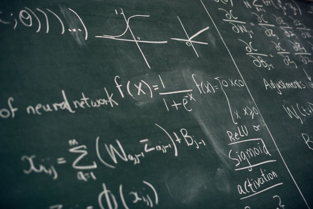 Formulas and numbers from the field of machine learning written in white chalk on a blackboard