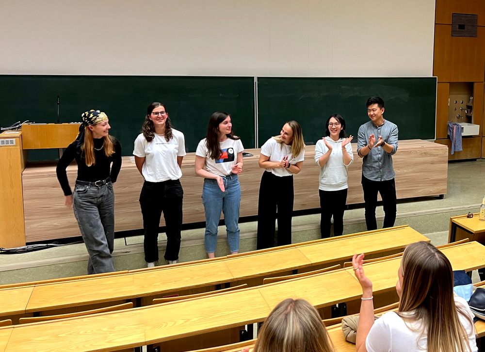 Six young researchers stand in front of a blackboard in a lecture hall. They were the speakers of the science slam "Tübingen Talks Tech" on AI research.