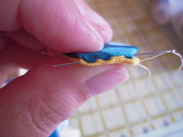 close up of hand stitching two English-Paper-Pieced hexies (EPP) together. One hexie is blue with polka dots and the other is yellow. A needle with thread is running through them. 