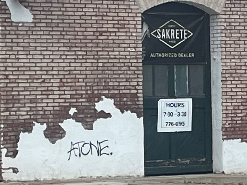 A brick wall and dark green door. On the wall is graffiti reading "ATONE."