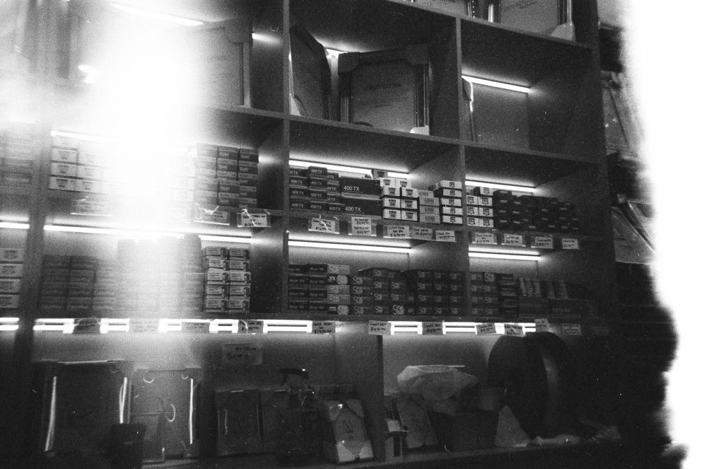 The last shot on the black and white disposable camera, showing boxes of film on the shelves in Photolife. Light leaks shoot down like funnel clouds on either side.