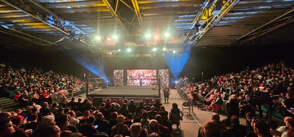 A wide shot of the Doncaster Dome set up for Revolution Pro Wrestling's  High Stakes 2025 event. The photographer is seated roughly six rows up in one of the three rakes of tiered seats that surround the ring. The wrestlers entrance is on the fourth side.