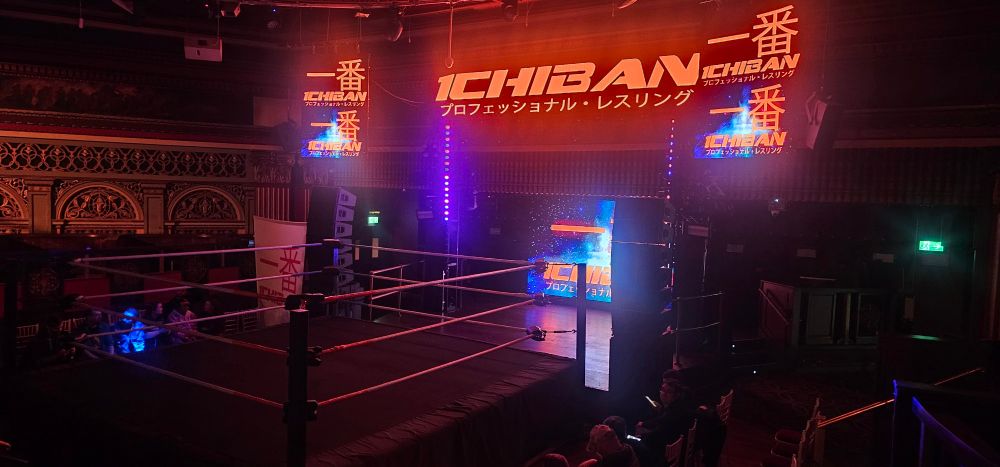 A shot of the setup for ICHIBAN Wrestling at PRYZM in Kingston upon Thames. A more intimate setting than most, there are a handful of ringside chairs with the ring adjoining the stage. The photo was shot on a balcony overlooking the ringside area.