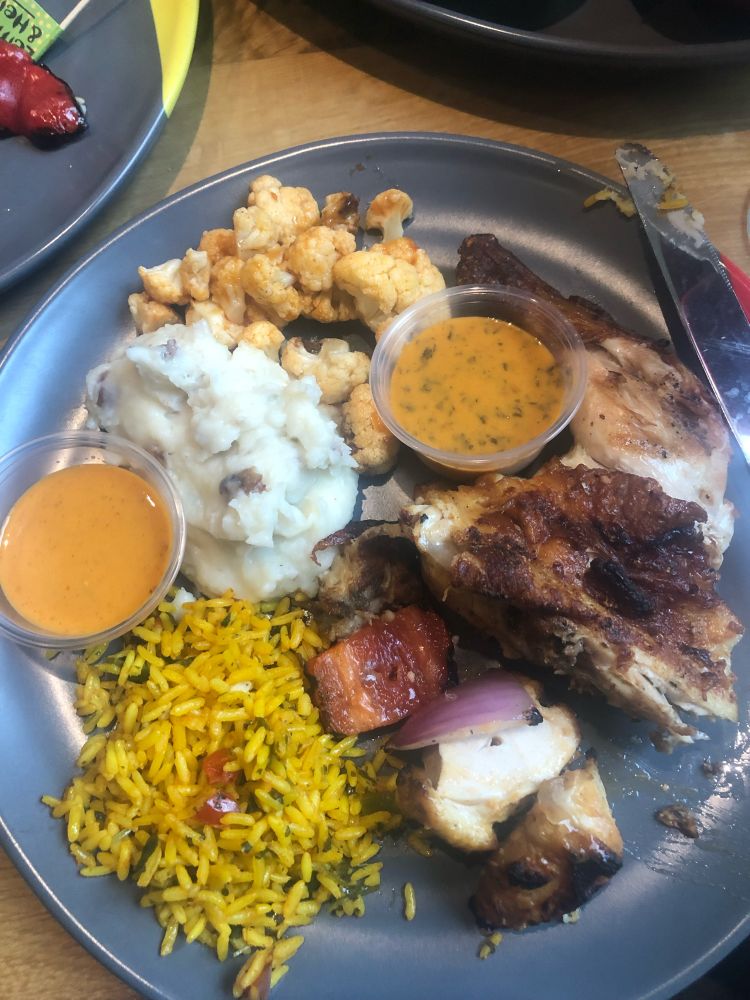 A plate with rice, potatoes, chicken and cauliflower on it. With 2 orange colored sauces on the plate.  