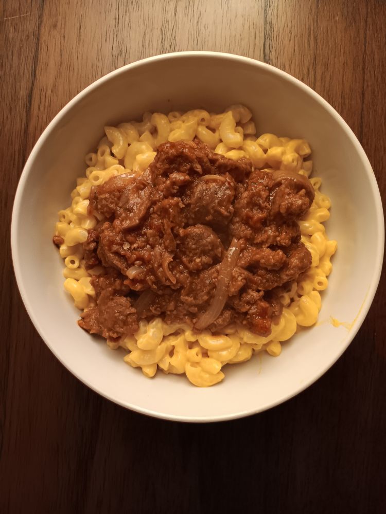 a bowl of mac and (vegan) cheese topped with red sauce with (vegan) sausage