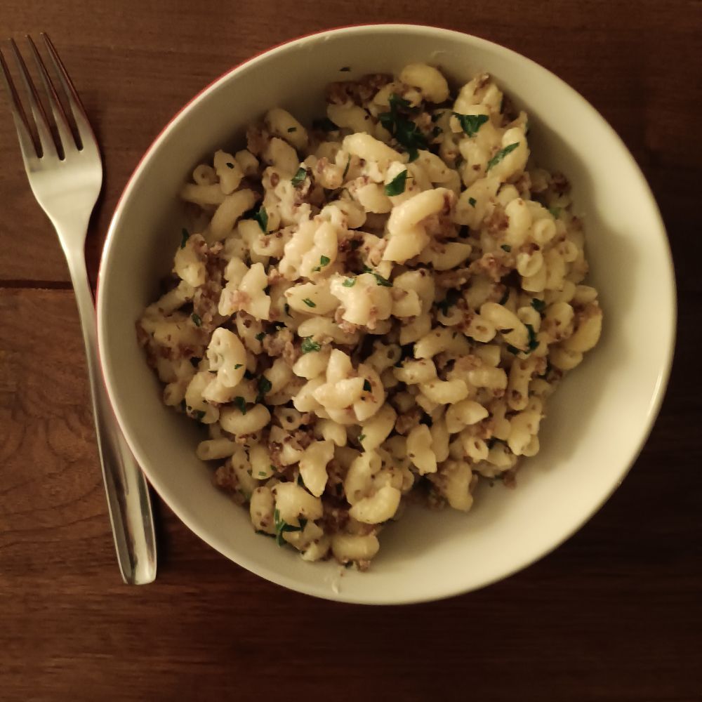a bowl of mac and cheese with brown and green bits in it. a fork is to the left of the bowl