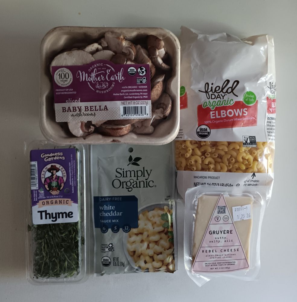 ingredients set out on a white background: sliced mushrooms, elbow macaroni noodles, Rebel Cheese vegan Gruyère, dairy-free white cheddar sauce mix, fresh thyme