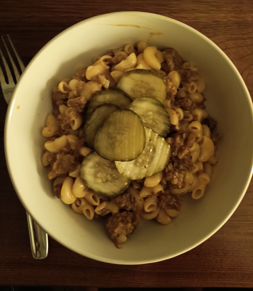 a bowl of mac & cheese with vegan sausage mixed in, with some pickle slices on top