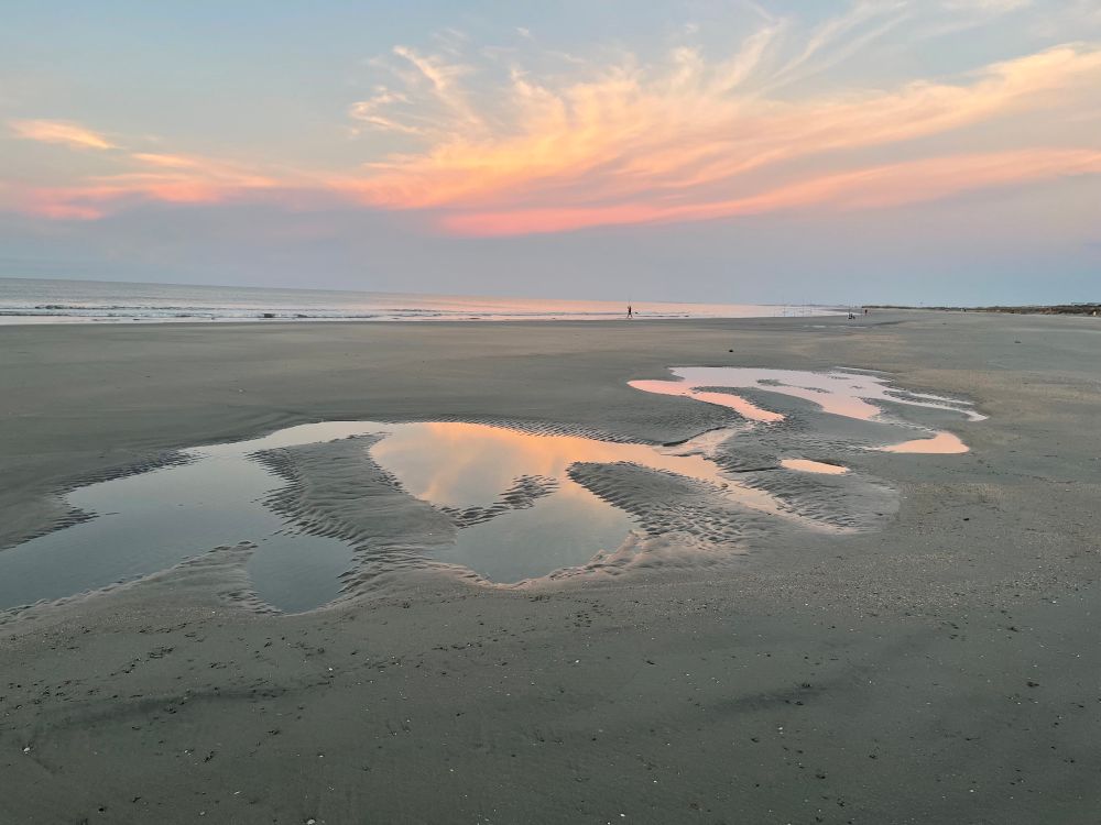 A picture of the reflection of the sunrise on tidal pools with the colors of peach and sky blue on wet sand. 