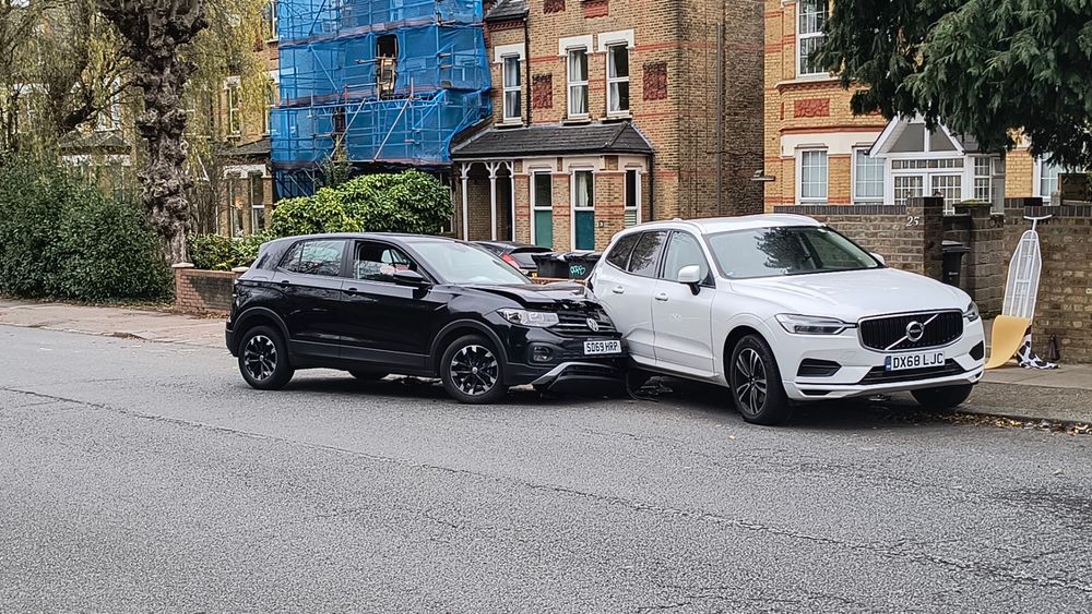 Black volkswagen wheels turned kerbside has smashed into the rear offside corner of a white volvo. The volkswagen has suffered extensive damave to the left bonnet and front.