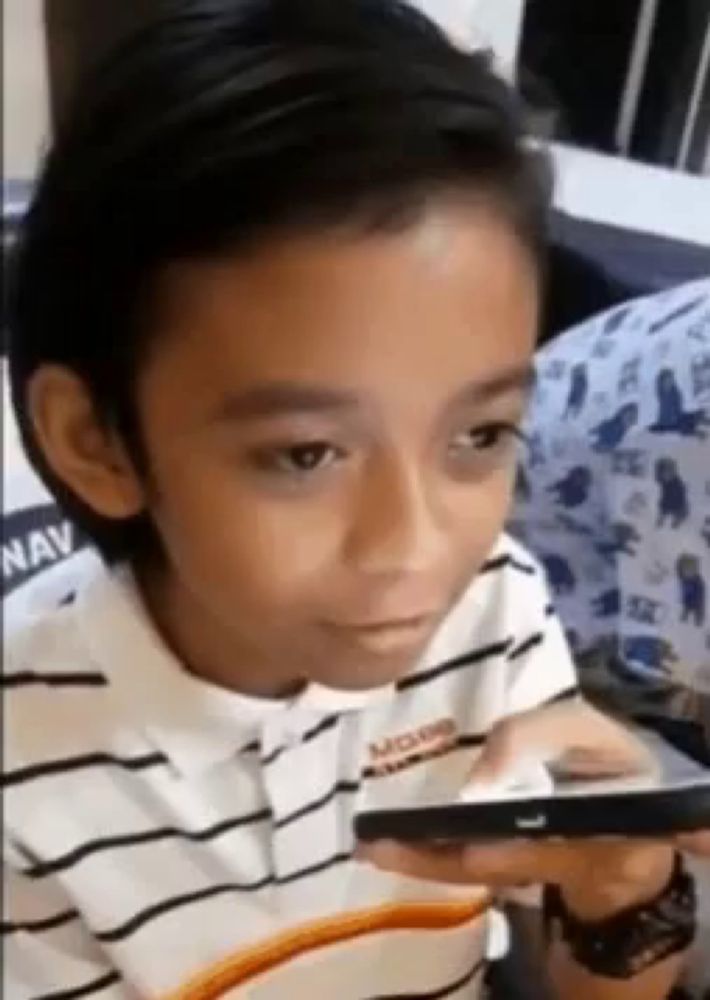 a young boy is looking at a cell phone while wearing a striped shirt .