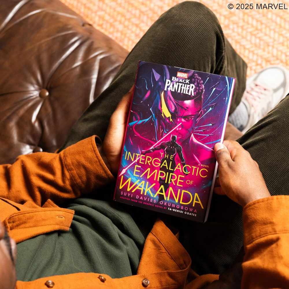 The hands of a Black person holding, front cover & face up, the book, Black Panther: The Intergalactic Empire of Wakanda by Suyi Davies Okungbowa.