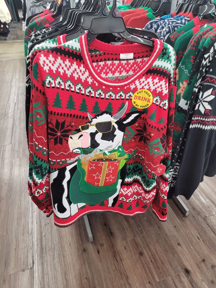 A sweater depicting a cow holding a present. The present functions as a pocket, and there is a sticker on the sweater which says, "Put your drink in ly pouch."