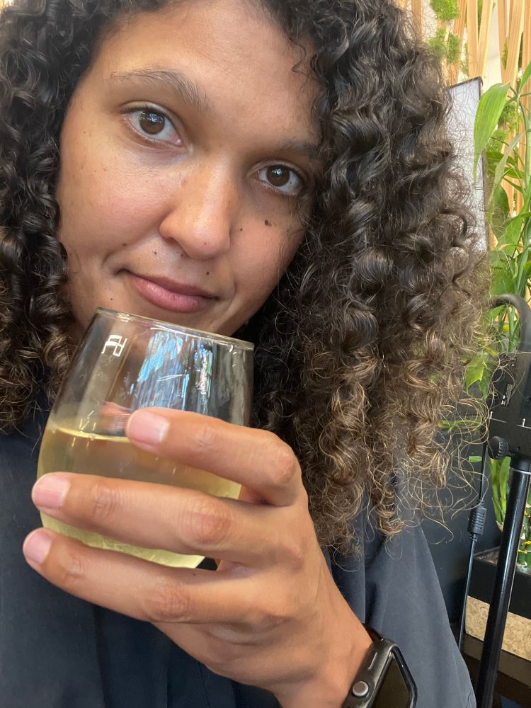 Me with dry curly hair down and holding a glass of white wine 