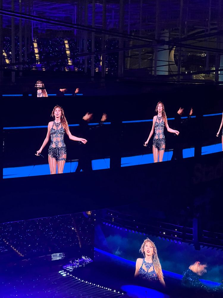 Taylor Swift wearing a sparkly midnights bodysuit with the torso cutouts with her arms out.