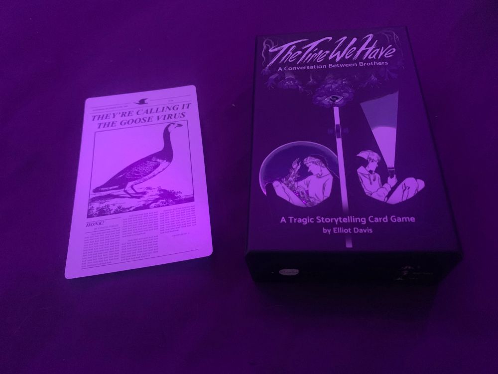 A purple-lighting photo of The Time We Have, a ttrpg by Eliot Davis. Next to it is a card with an image of a goose stylized in newsprint. The headline reads ‘They’re calling it the Goose Virus.’