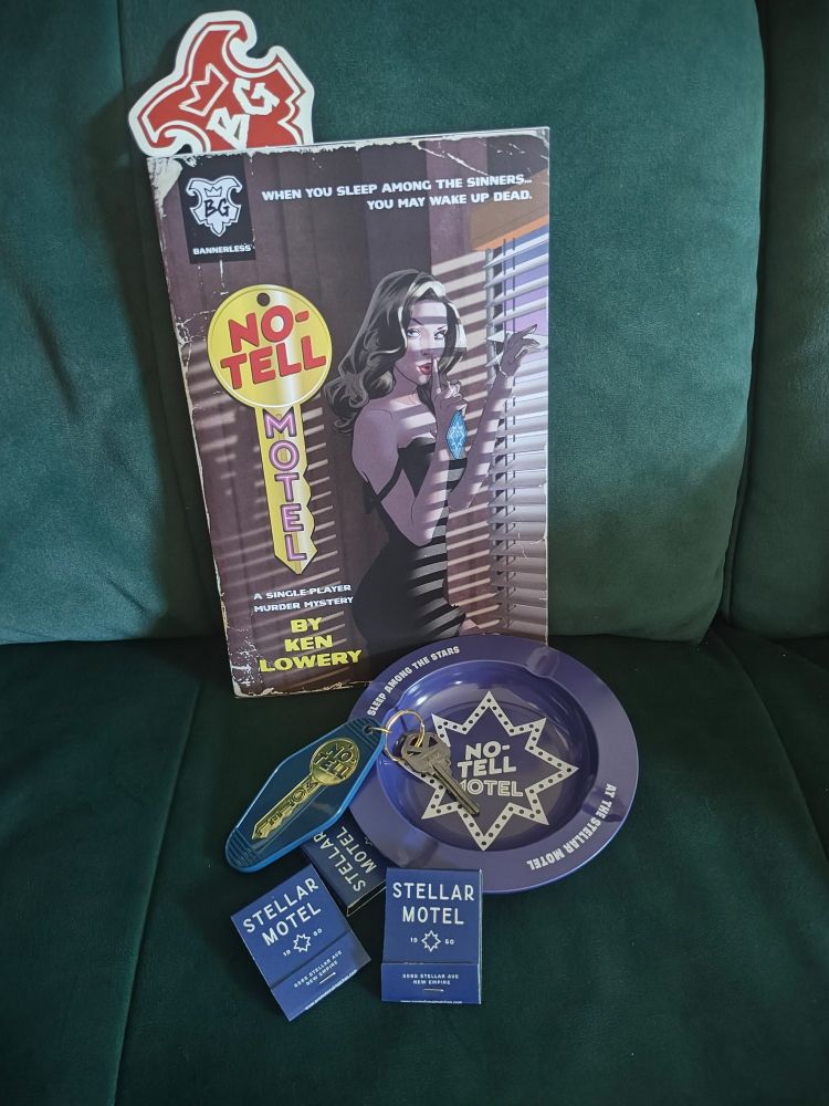 No-tell Motel physical copy with flavor objects, motel ashtray, matches and room key Stellar Motel on a millennial green velvet couch.