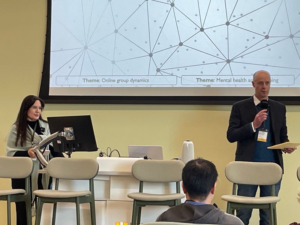 Two people stand in front of a screen with an image of dots and lines. 