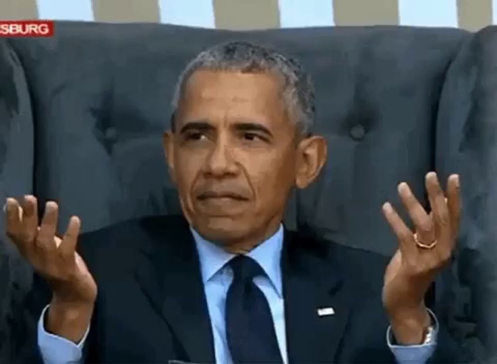 a man in a suit and tie is sitting in a chair with his hands up .