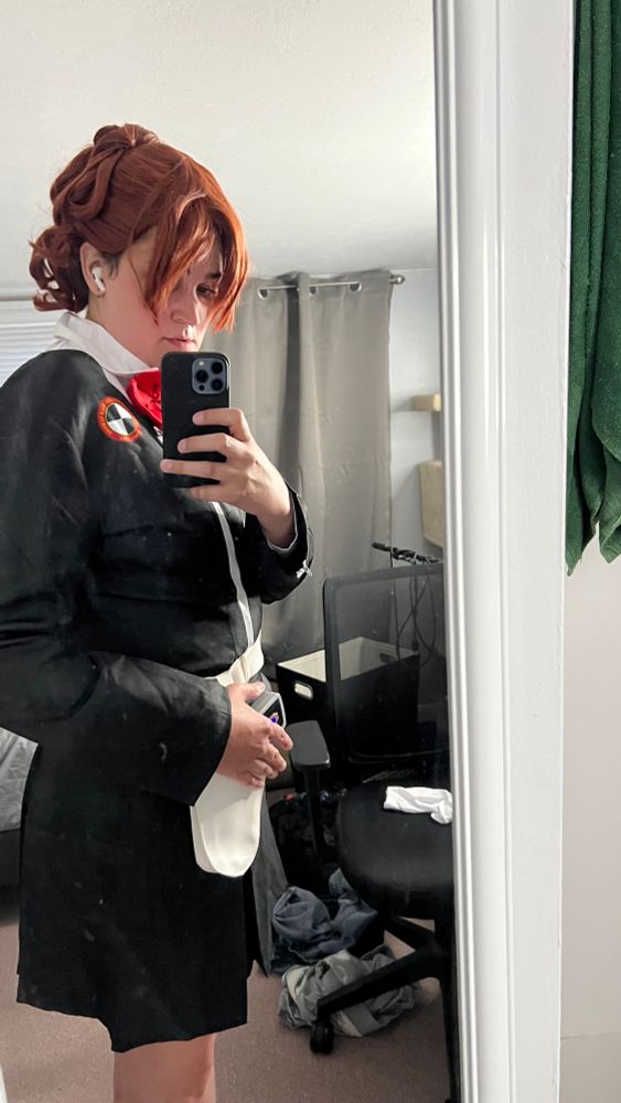 Kotone Shiomi cosplay from Persona 3 Portable. Picture is taken with an iPhone pointed to a mirror. Mostly black outfit with a red armband and red bow. The hair is a red wig and is styled up in a ponytail and some curls. There is a belt with an evoker, a prop that looks like a gun. 