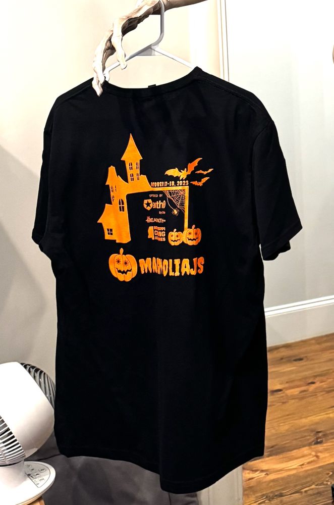 Back of the MagnoliaJS 2023 shirt with a haunted house, bats, and the spooky magnolia logo. It also has our three sponsors from that year and the date.