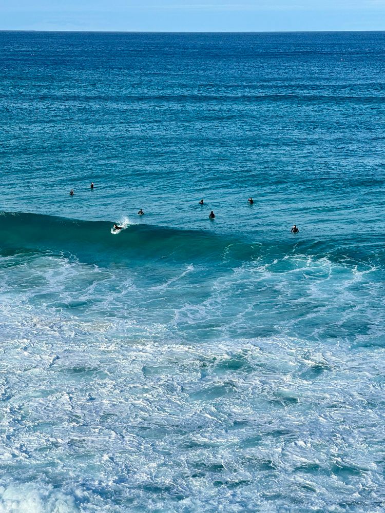 blue ocean with distant people, like dark seals, in the surf.