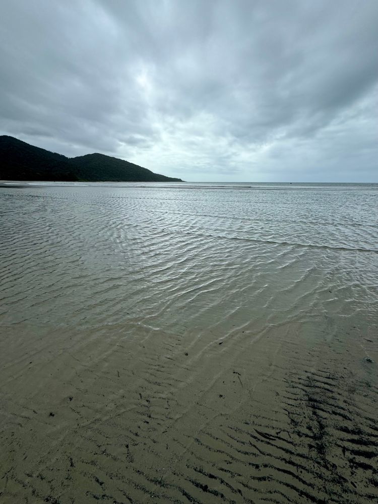 a vast shallow silvery tide washes in front of a dark promontory in the distance 