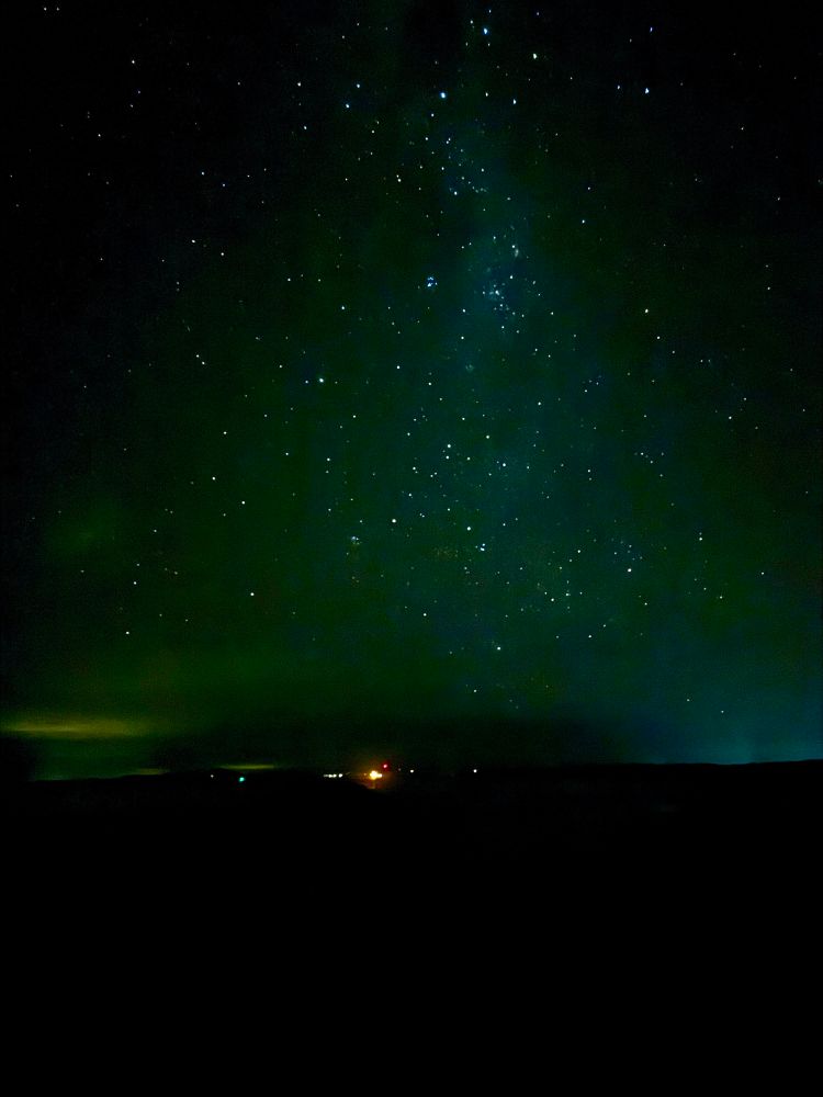 stars in a dark blue-green night sky, over distant lights