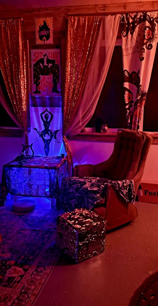 Green chair with fabulous sparkly ottoman angled perfected off to the right side.  Left shows a table lite feom underneath to highlight the World Goddess on the wall. Above are two pieces of canvas art, one says "sit like a lady" and shows a woman defiantly manspreading her legs and the second above that shows a flame and says "exist loudly"