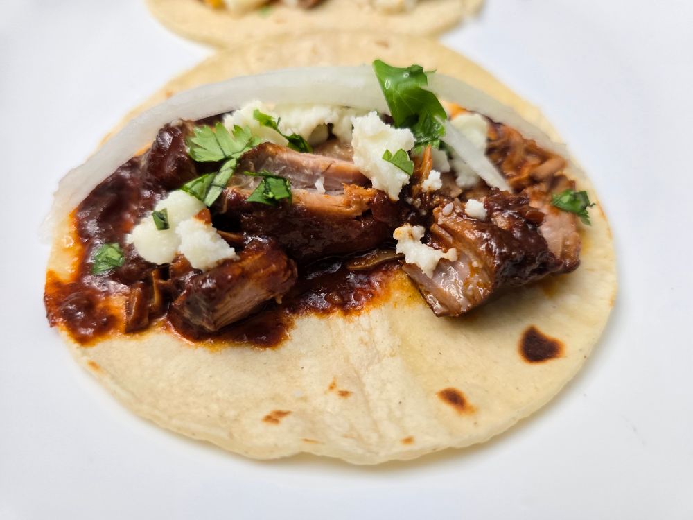 photo of the adavata meat shredded on a toasted corn tortilla topped with queso fresco, cilantro, pickled onion, and lime