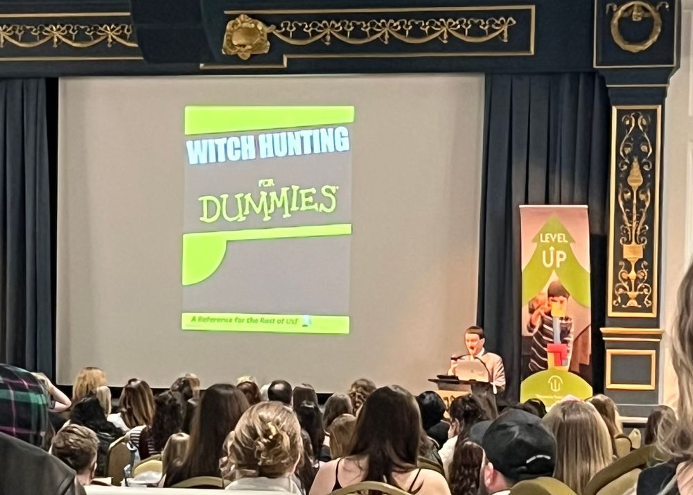 Author Grady Hendrix speaking at a podium while a fake book cover titled Witch Hunting for Dummies is projected next to him.
