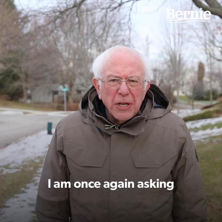 Bernie Sanders in a grey coat outside in the winter talking to the camera. It is a meme image.