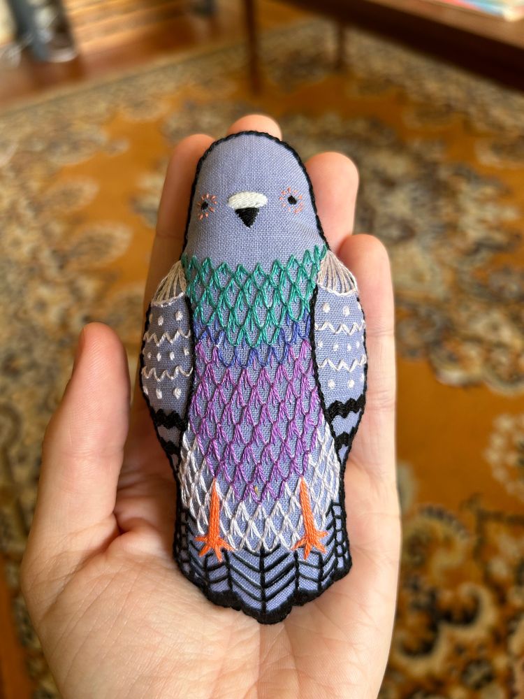 An embroidered pigeon plushie sitting in the poster’s hand