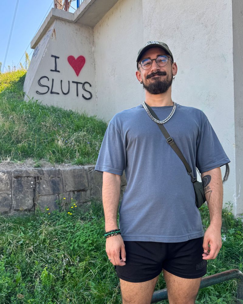 Dizzy smiling and standing in front of graffiti that reads "I love sluts"