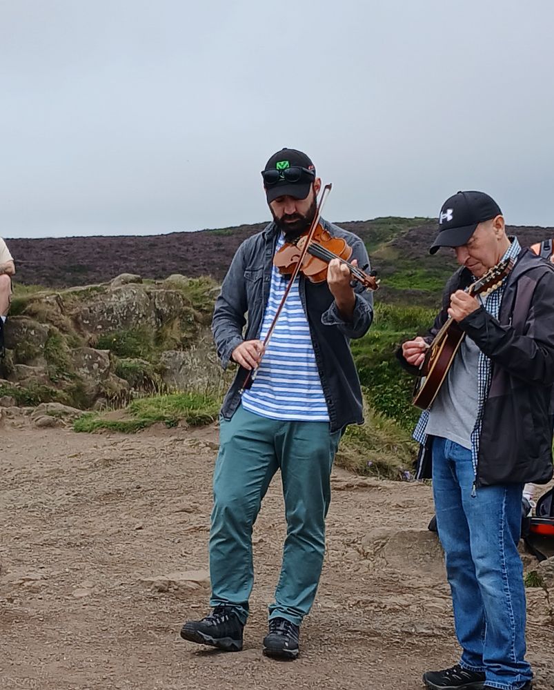 Two musicians playing on top of Cavehill, one with a fiddle and the other with a stringed instrument that resembles a mandolin or bouzuki or somesuch