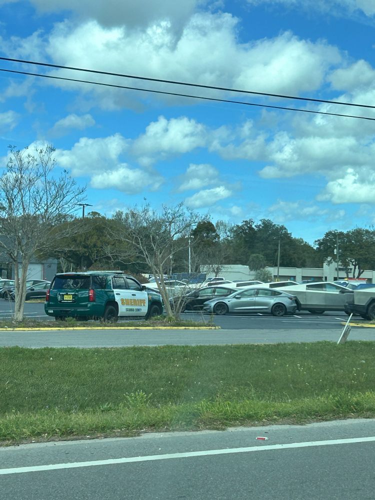A sheriff’s deputy car guards rows of Teslas at an unopened dealership in Pensacola, Fl 