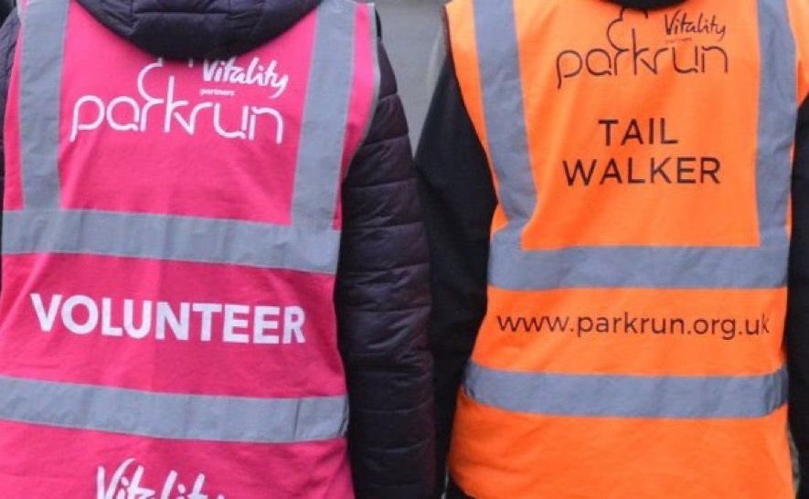 Two park run tabards on the back of volunteers - pink on left, orange on the right for tail walker.