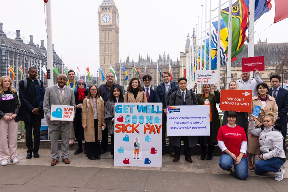 Campaigners stand outside in Parliament Square, with Big Ben in the background and the Giant get well soon card in front. Campaigners hold signs from MS Society, Leukeamia Care and Organise. Credit: Sylvie Pope Photography, Safe Sick Pay campaign
