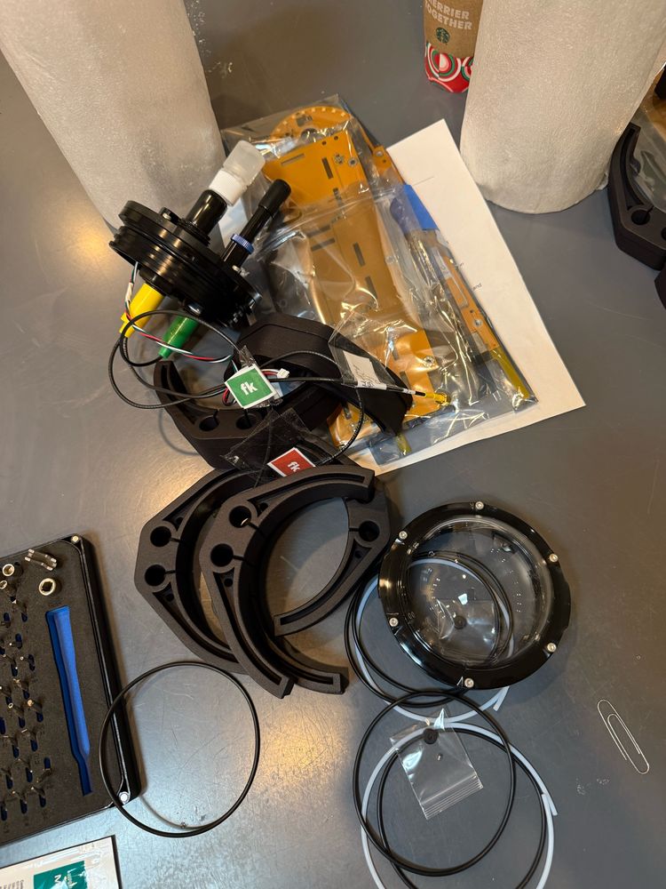 A closeup of unassembled parts of a FieldKit.org underwater sensor sitting on a table, including clamps, gaskets, probes, and circuit boards. 