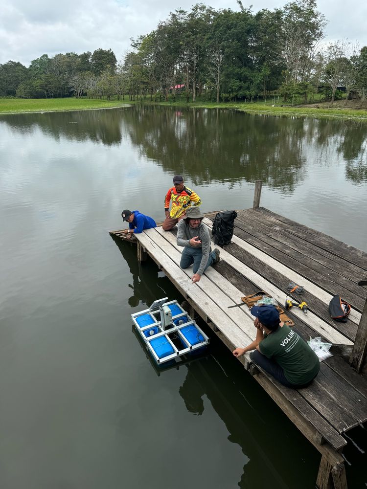 A group of people sit on a dock to deploy an environmental sensor in a lake in the Amazon basin. 