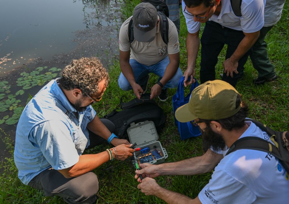 Workshop attendees configure a FieldKit water quality station next to a pond before deployment. 