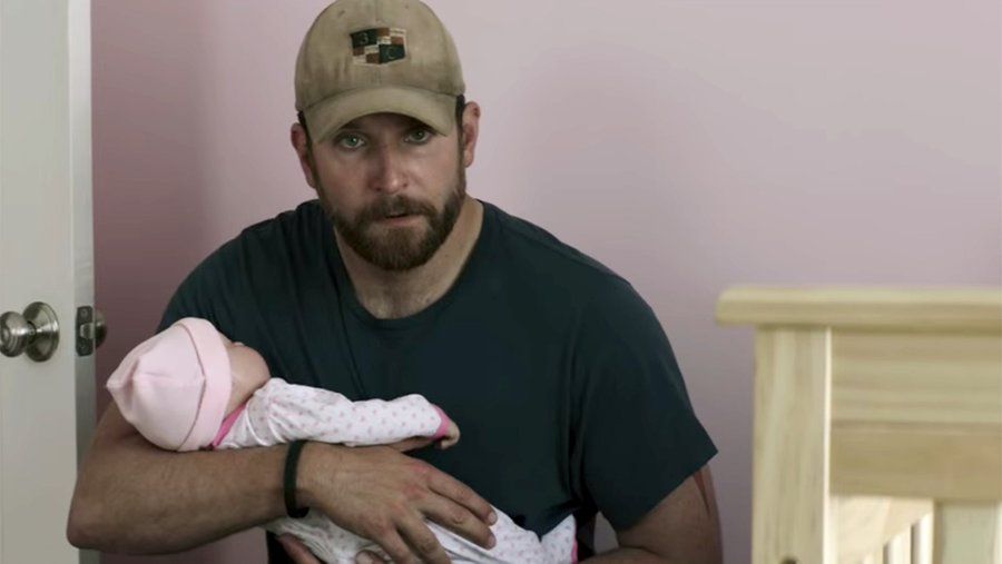 Man in a beige cap and black T-shirt holding a clearly fake baby doll.