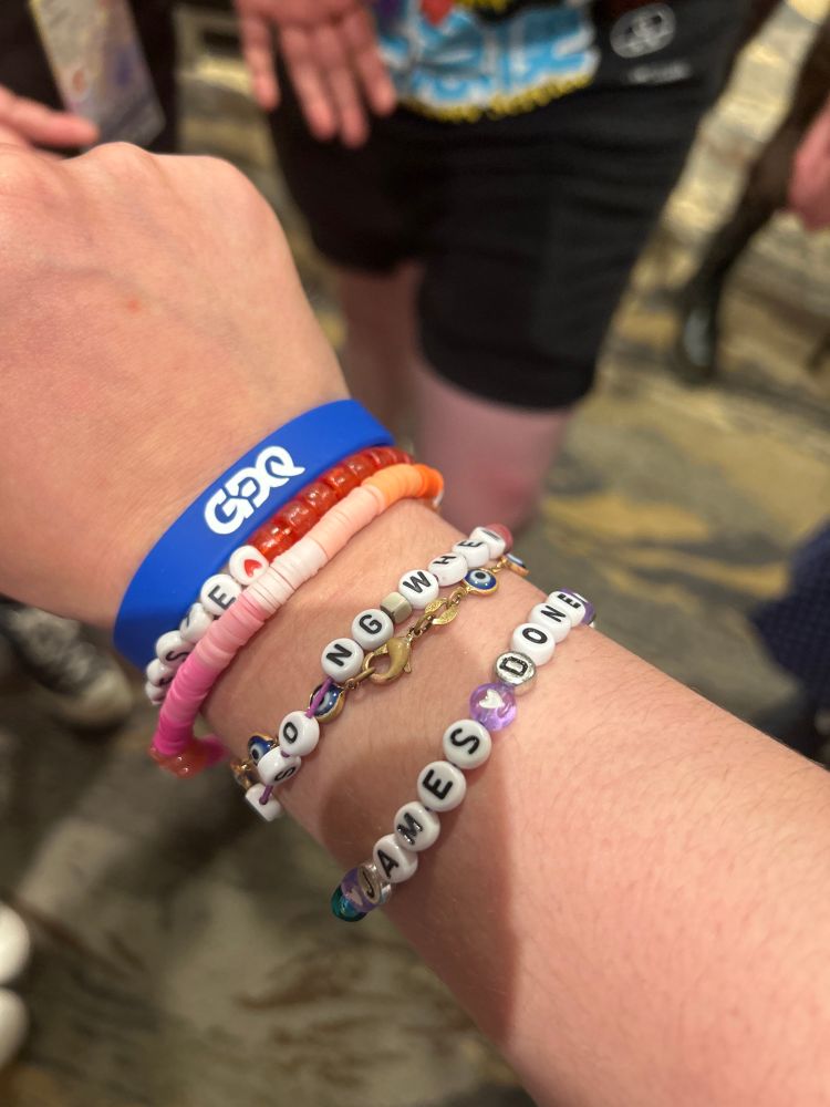Photograph of wrist with multiple friendship bracelets on, with one having the words James Done Quick.