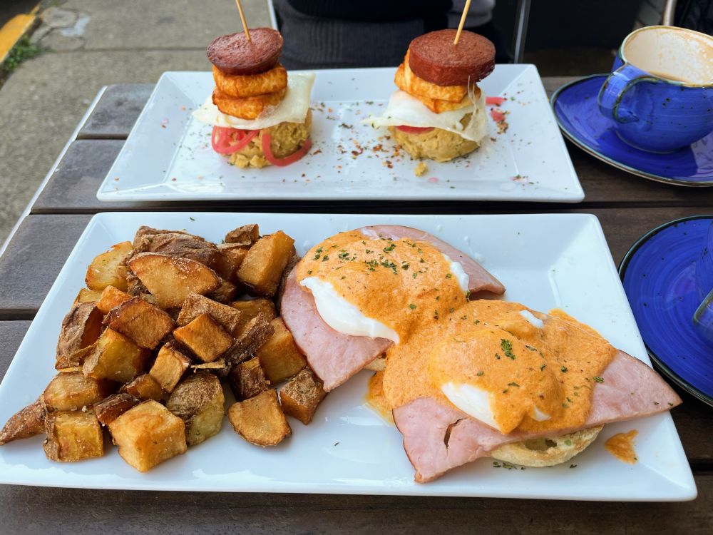 At the top, Mangu Sliders on a rectangular plate. Mashed plantains on the bottom followed by pickled onions, fried eggs, fried cheese, and topped with sausages. A toothpick holds the stack together.

On the bottom is Eggs Benedict with bistro style potatoes on the side. Fresh Canadian Bacon, 2 softly Poached eggs with hollandaise sauce on an English muffin.