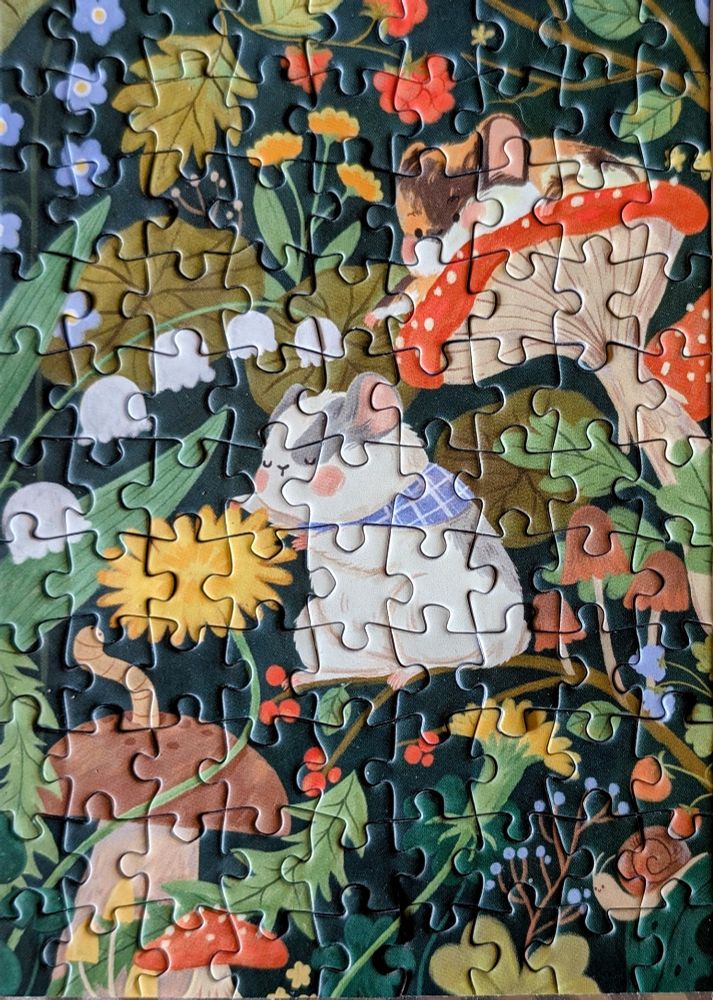 A small jigsaw puzzle featuring two chonky field mice surrounded by colorful mushrooms, dandelions, lily of the valley, berries, and leaves.