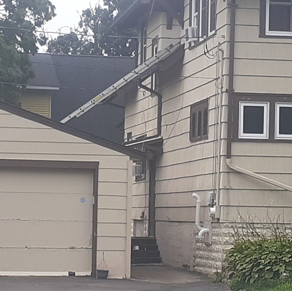 Ladder going from sloped roof of a garage over an overhang onto a house.